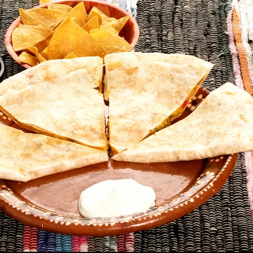 Four quesadilla slices and a dollop of sour cream on a brown plate, with tortilla chips.