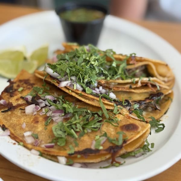 Three golden-brown birria tacos topped with cilantro and diced red onions, with lime wedges and salsa.