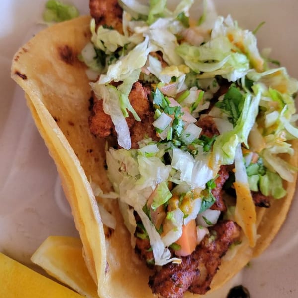 A close-up of a Taqueria Viva México taco filled with meat, lettuce, salsa, and a lemon wedge.