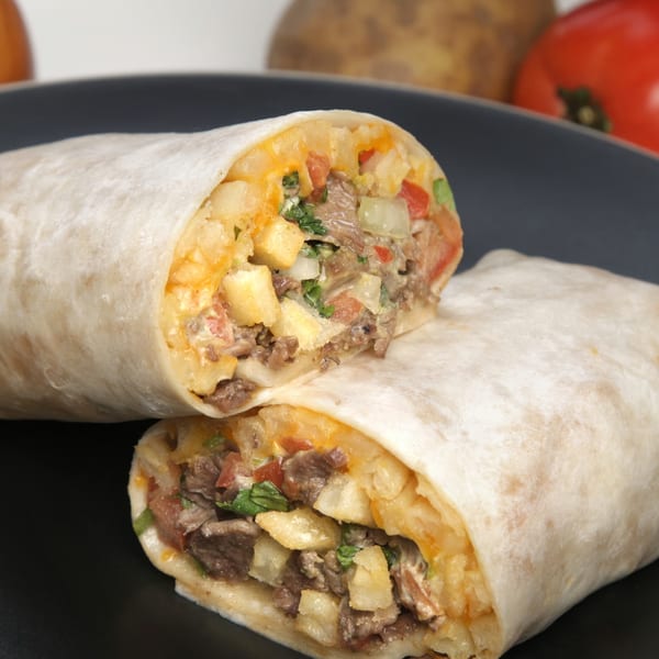 A large Mexican burrito, cut in half, revealing steak, potatoes, cheese, and vegetables.
